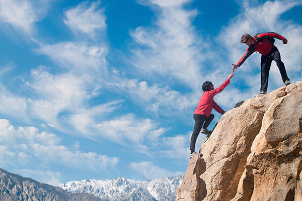 Photo of one person helping another up a mountain.
